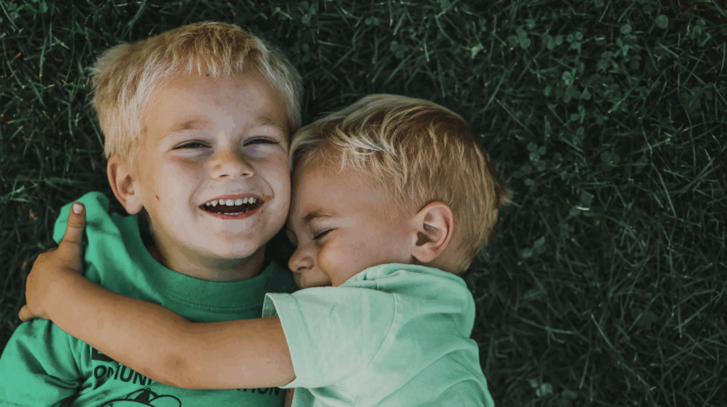 Two young boys smiling and hugging on green grass, representing family joy and connection, relevant to private adoption themes.