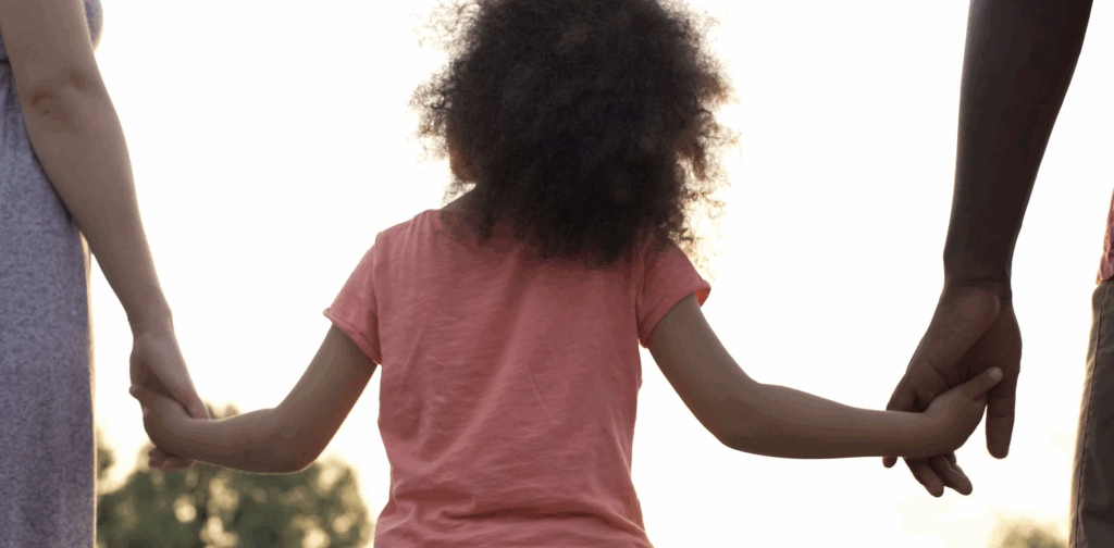 Family holding hands with a child in a pink shirt, symbolizing love and connection in the adoption journey in Texas.