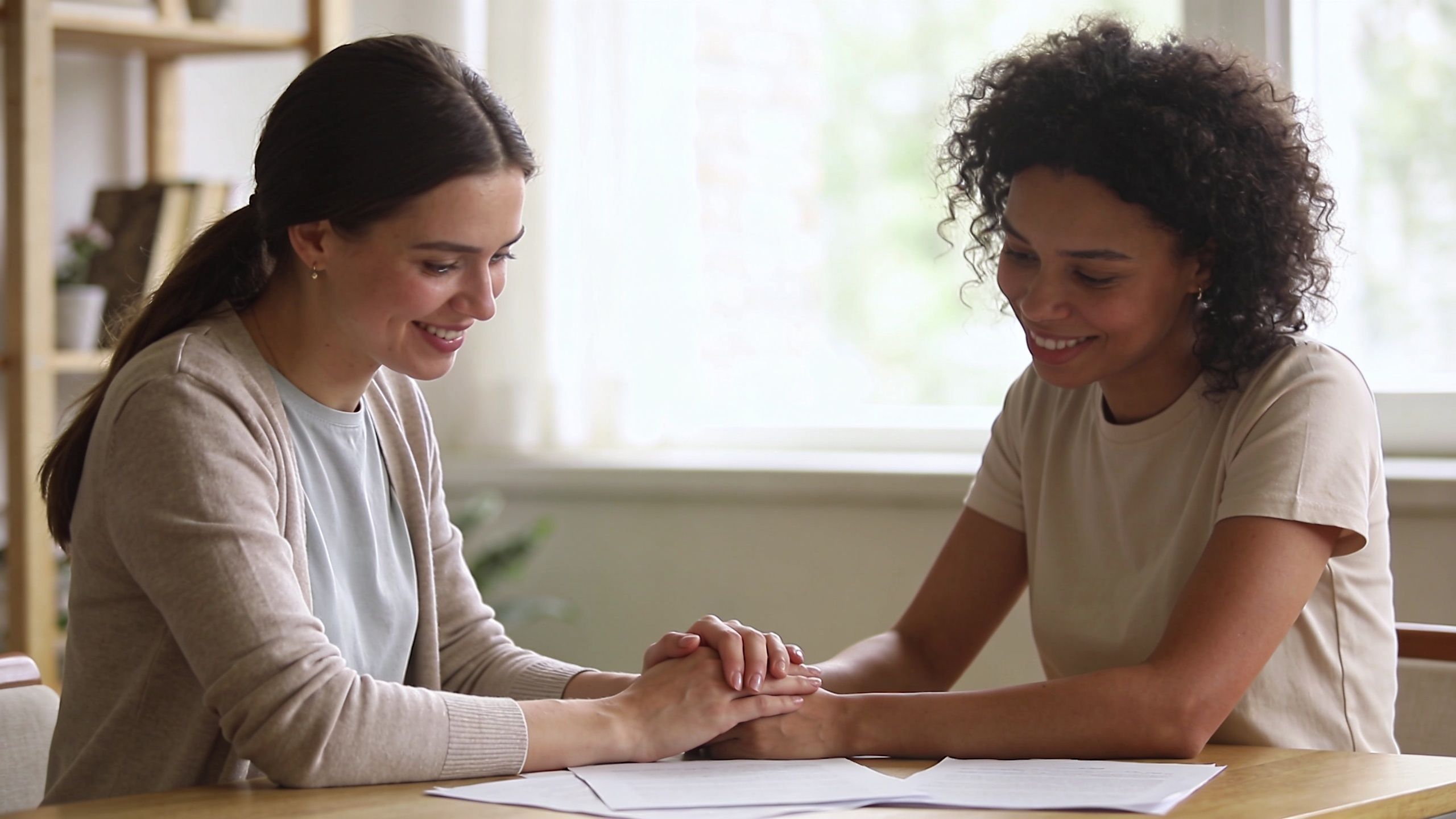 A supportive woman holding hands with another woman while looking at legal documents together at a table.