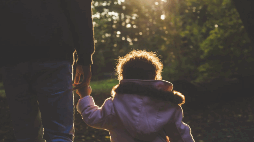 Parent and child walking hand in hand in a sunlit park, symbolizing the joy of adoption and family connections in Texas.