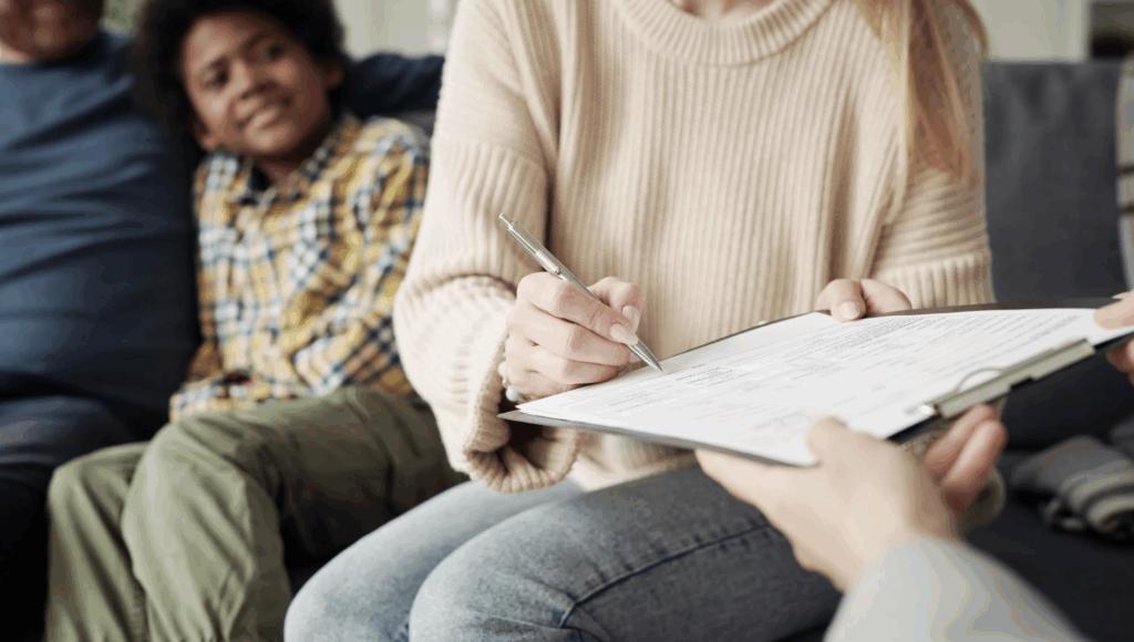 Woman signing adoption paperwork with a child smiling in the background, illustrating the process of adopting from foster care in Texas.