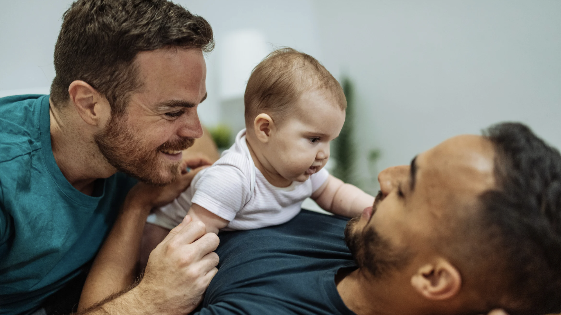 Two fathers joyfully interacting with their infant child, emphasizing family bonding and love in a home setting, relevant to adoption discussions in Texas.