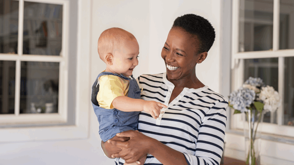 Smiling woman holding baby in a home setting, illustrating kinship adoption and family connections in Texas.