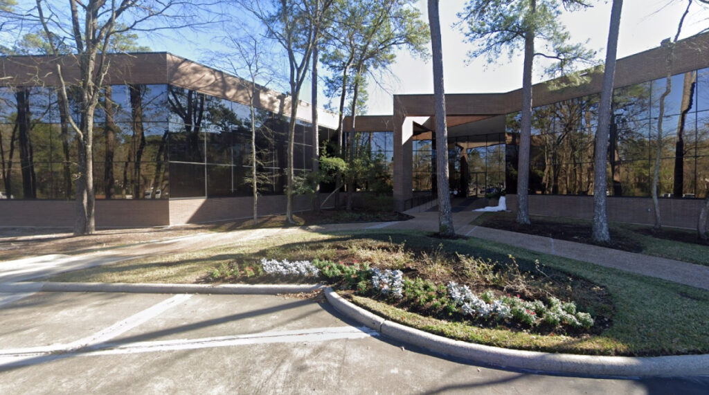 Modern law office building in Kingwood, Texas, featuring large glass windows, surrounded by trees and landscaped flower beds, representing the Law Office of Bryan Fagan's commitment to family and adoption services.