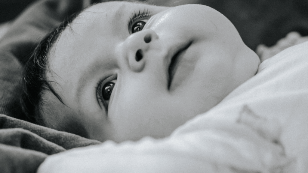 Baby looking up with curious expression on a soft surface, symbolizing the innocence and new beginnings often associated with adoption.