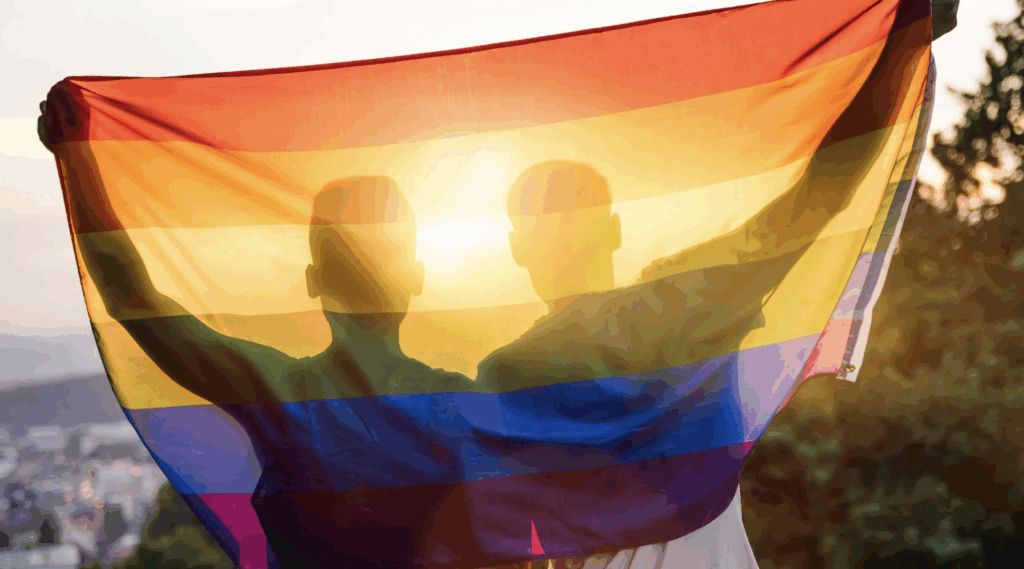 Couple holding a rainbow flag, symbolizing LGBTQ+ pride and acceptance, against a sunset backdrop, representing inclusivity in adoption rights in Texas.
