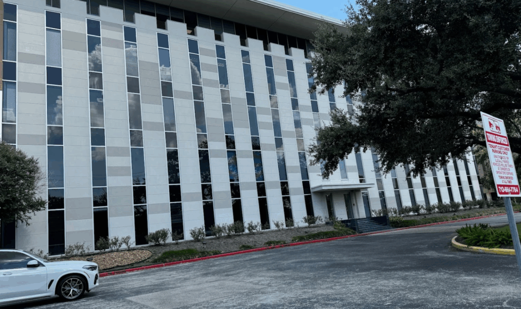 Modern office building exterior with large reflective windows, located in Houston, Texas, featuring landscaped surroundings and a parking area.