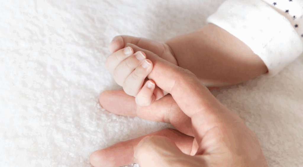 Adult hand holding a baby's hand, symbolizing love and connection in the context of adoption and legal guardianship in Texas.